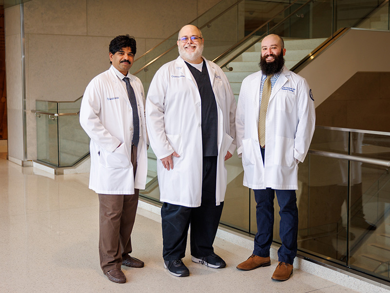 Three Radiation Oncology residents standing inside the School of Medicine near a flight of stairs.